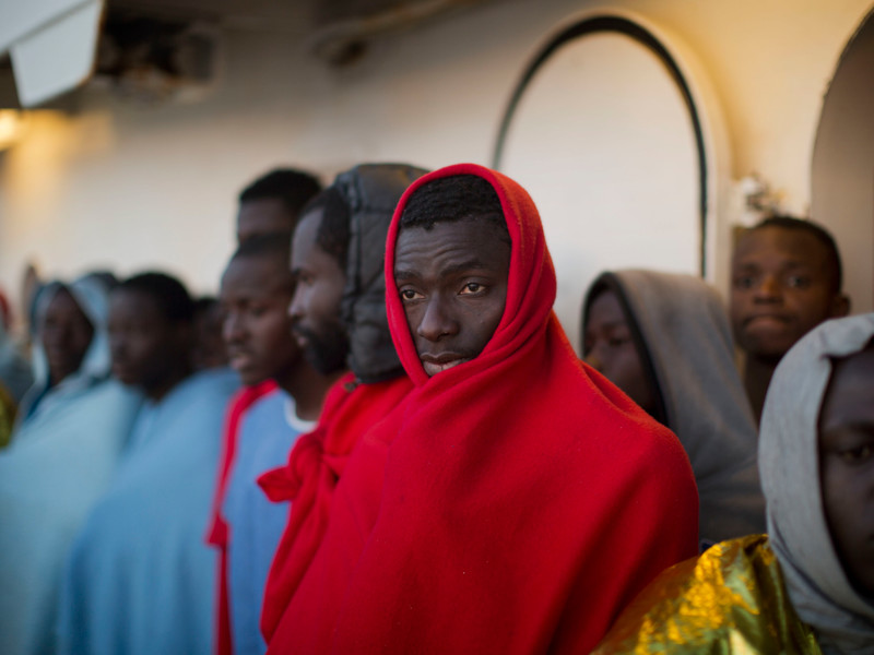 In Decken gehüllt, stehen Migranten aus Subsahara-Staaten und blicken auf die Küste im Inneren des Rettungsschiffs Golfo Azzurro, als sie im Hafen von Messina in Italien ankommen. 