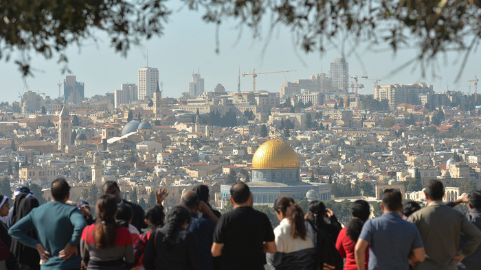 Menschen stehen auf dem Ölberg in Jerusalem und blicken auf die historische Altstadt.