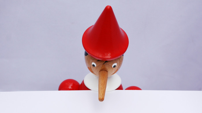 Pinocchio schaut mit gesenktem Kopf auf ein leeres Blatt Papier