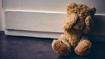 Teddybär sitzt vor der Tür und bedeckt seine Augen.