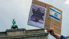 Plakat wir in die Höhe gehalten, im Hintergrund das Brandenburger Tor