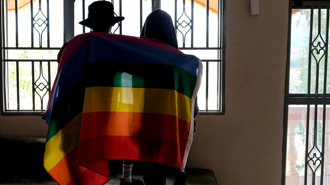 Ein Paar in Uganda bedeckt sich mit einer Regenbogen-Fahne uns sie sind von hinten zu sehen.