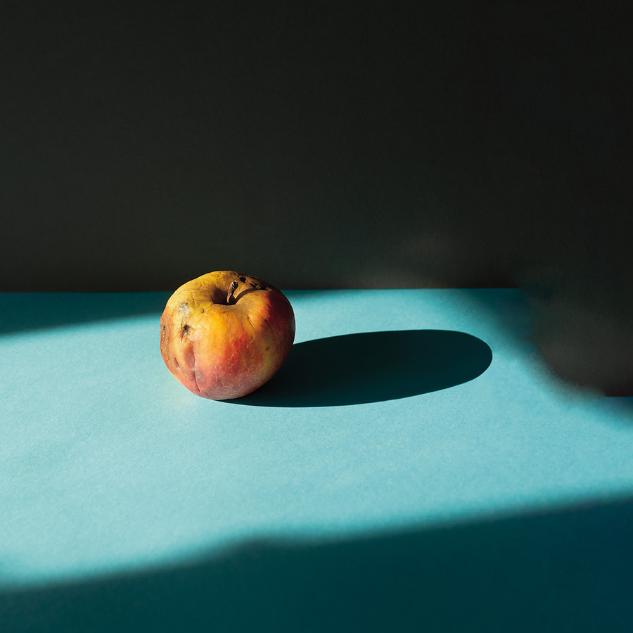 Apfel mit faulen Stellen im Lichtschein auf einem türkisfarbenen Untergrund