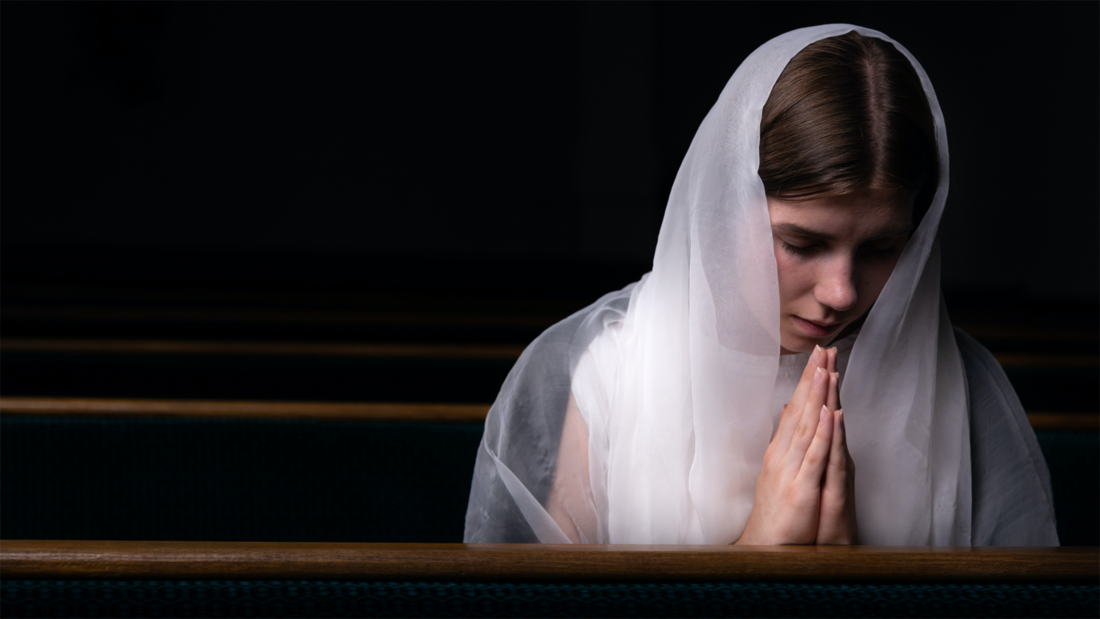 Eine Frau sitzt in einer Kirchenbank und betet.