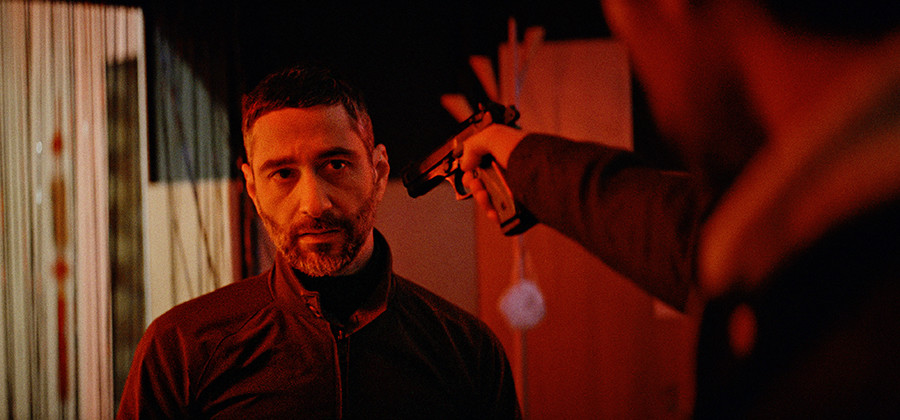 Filmszene aus "Schock" mit Denis Moschitto, der von einer Person mit einem Revolver bedroht wird