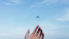 verschwommene Hand vor Himmel mit Fallschirm dahinter