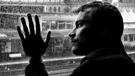 schwarz-weiß Bild, einsamer Mann schaut aus dem Fenster mit einer Hand an der Scheibe