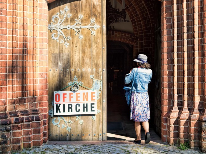 Eine Frau betritt eine Kirche, die mit einem Schild 'Offene Kirche' zum Besuch einlädt
