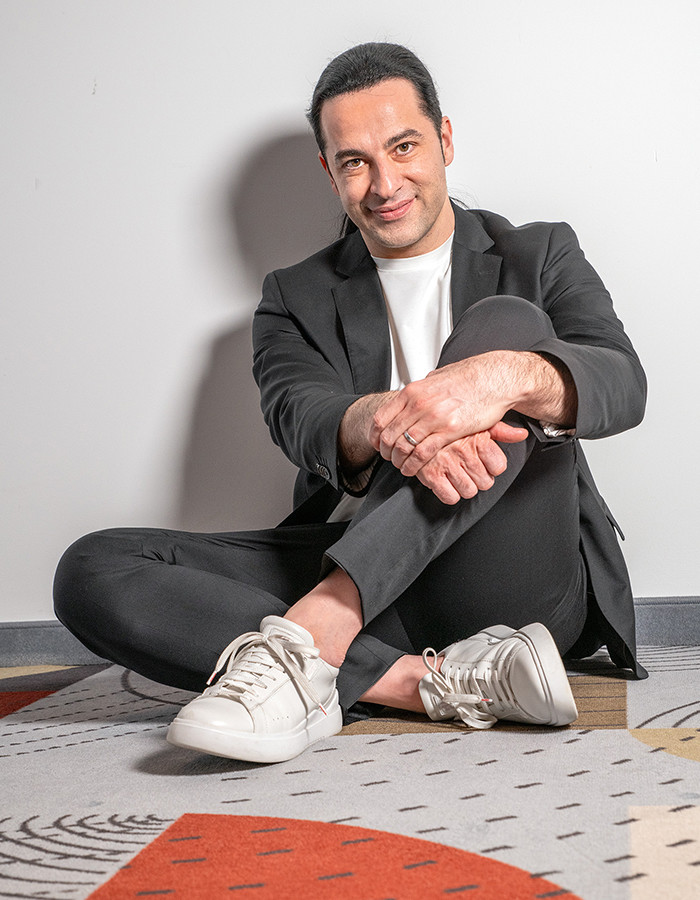 Comedian Bülent Ceylan sitzt auf einem gemusterten Teppich. Er trägt einen grauen Anzug: 2019 ließ Comedian Bülent Ceylan sich evangelisch taufen