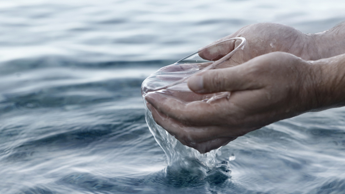Zwei Hände umfassen eine mit Wasser gefüllte Schale zur Taufe.