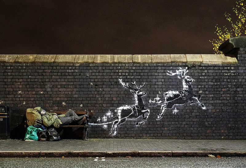 A Christmas Greeting from Ryan: ein Banksy in Birgmingham. Graffiti auf der Mauer, auf dem Rentiere die Bank mit einem Obdachlosen zu ziehen scheinen