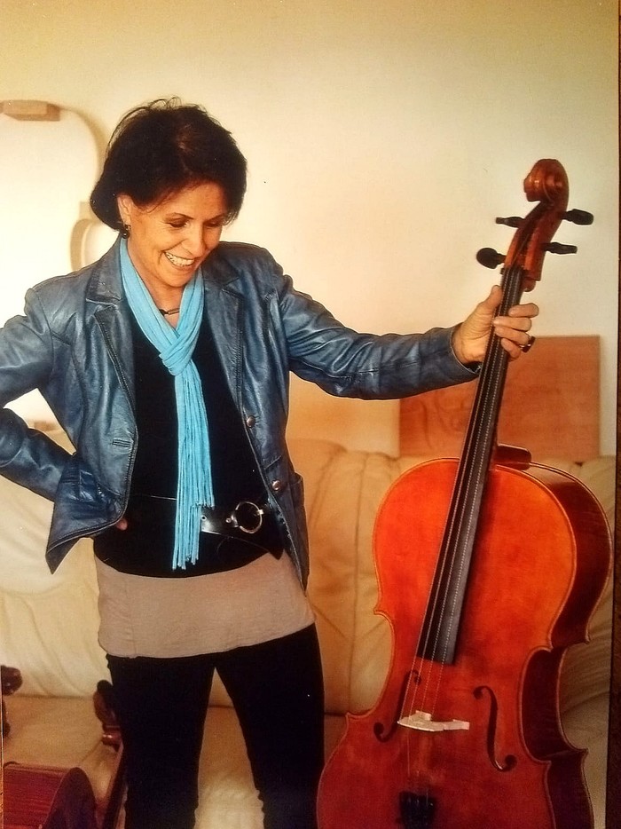 Eine Frau in blauer Jacke hält mit ihrer Hand ein braun-rotes Cello