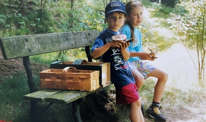 Zwei Kinder sitzen auf einer Bank mit gesammelten Pilzen in der Hand