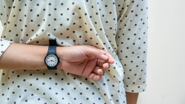 Eine Frau hält ihren Arm mit Armbanduhr hinter ihrem Rücken versteckt.