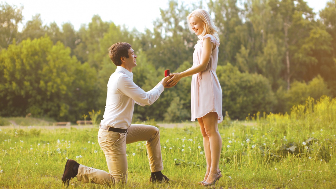 Ein Mann kniet vor einer Frau und macht ihr einen Heiratsantrag.