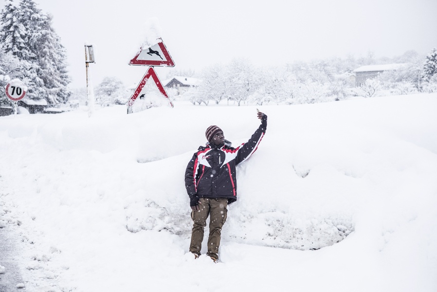 Ein dunkelhäutiger junger Mann schießt ein Selfie vor einer Schneeanhäufung.