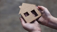 Hände halten ein Haus aus Pappe.