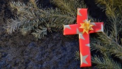 Ein Kreuz aus weihnachtlichem Geschenkpapier liegt auf einem Tannenzweig. 
