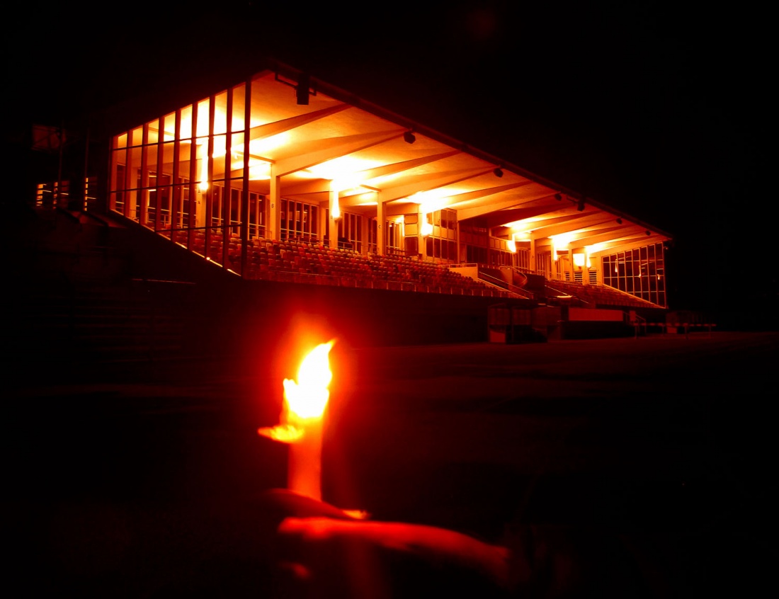 Schweinfurter Willy-Sachs-Stadion beleuchtet, im Vordergrund eine Hand, die eine Kerze hält.
