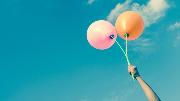 Hand mit zwei Luftballons vor blauem Himmel.