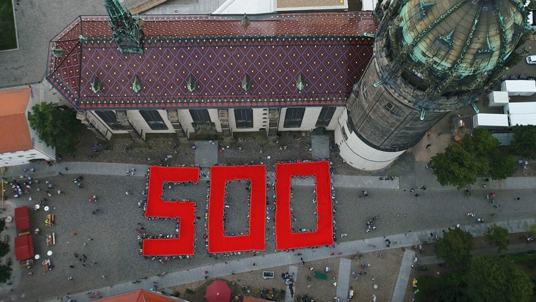 Luftbild einer von Menschen gehaltenen roten Ziffer 500 vor der Schlosskirche in Wittenberg, die auf das bevorstehende Reformationsjubiläum am 31.10.2017 hinweisen soll.