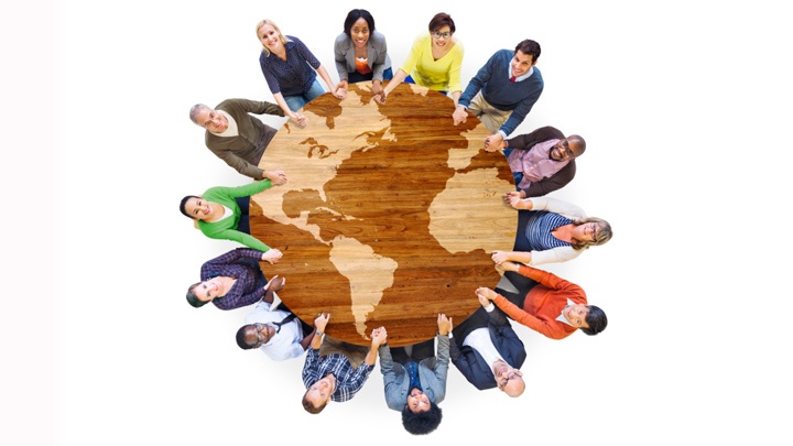 Eine Gruppe von Menschen verschiedener Nationen sitz um einen Tisch in Form einer Weltkugel. 