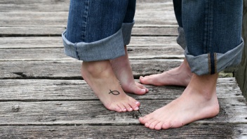 Eine Frau mit einem Ichthys-Tattoo auf dem Fuß steht auf den Zehenspitzen, um einen Mann zu küssen.
