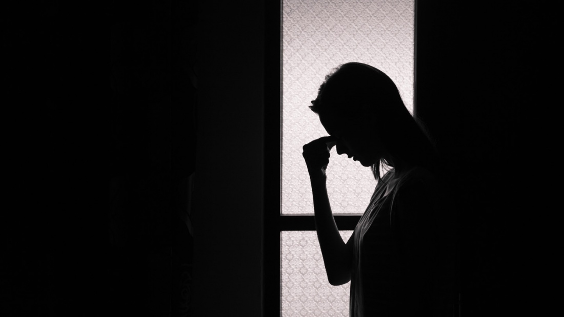 Eine Frau steht mit gesenktem Kopf in einem dunklen Raum.