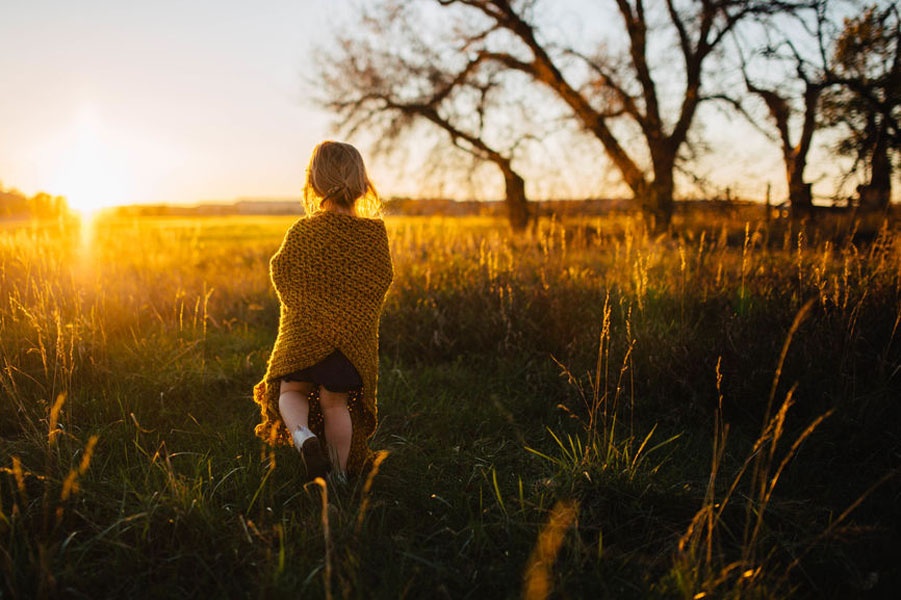 Ein Mädchen steht auf einem Feld und guckt nachdenklich in den Sonnenuntergang.