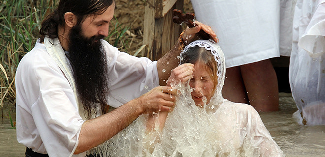Ein russisch-orthodoxer Pfarrer tauft ein junges Mädchen im Jordan 