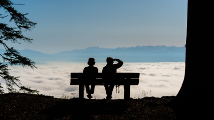 Zwei Personen auf einer Bank blicken auf ein Wolkenmeer