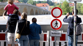 Menschen schauen sich in der Altstadt am Donauufer hinter einer Schutzwand das Hochwasser an. 