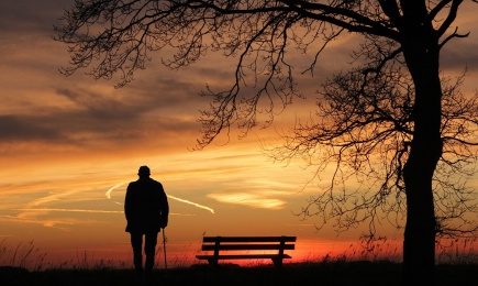 Älterer Mann auf einem Stock gestützt schaut sich einen Sonnenuntergang an