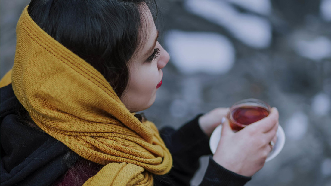 Iranische Frau mit lockerem Kopftuch trinkt Tee