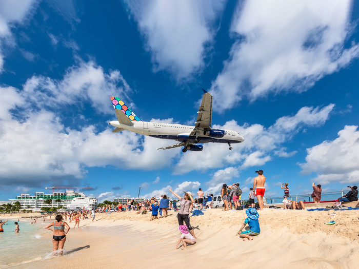 Maho Beach, Saint Martin: Ein Verkehrsflugzeug nähert sich dem Flughafen Princess Juliana über den Schaulustigen. Auf der kurzen Landebahn können die Strandbesucher die Flugzeuge aus nächster Nähe beobachten