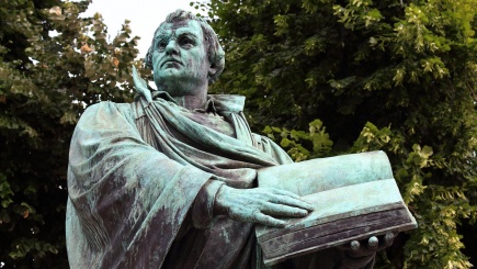 Statue von Martin Luther mit Bibel in der Hand vor einem Wald
