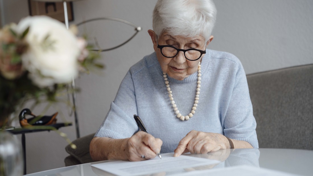 Seniorin schreibt etwas auf ein Blatt Papier