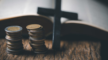 Geldstapel vor Kreuz und Bibel