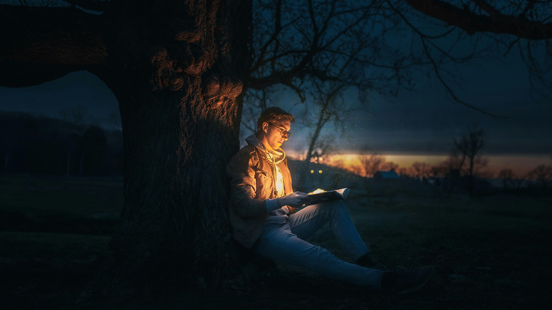 Mann liest im Dunkeln unter Baum