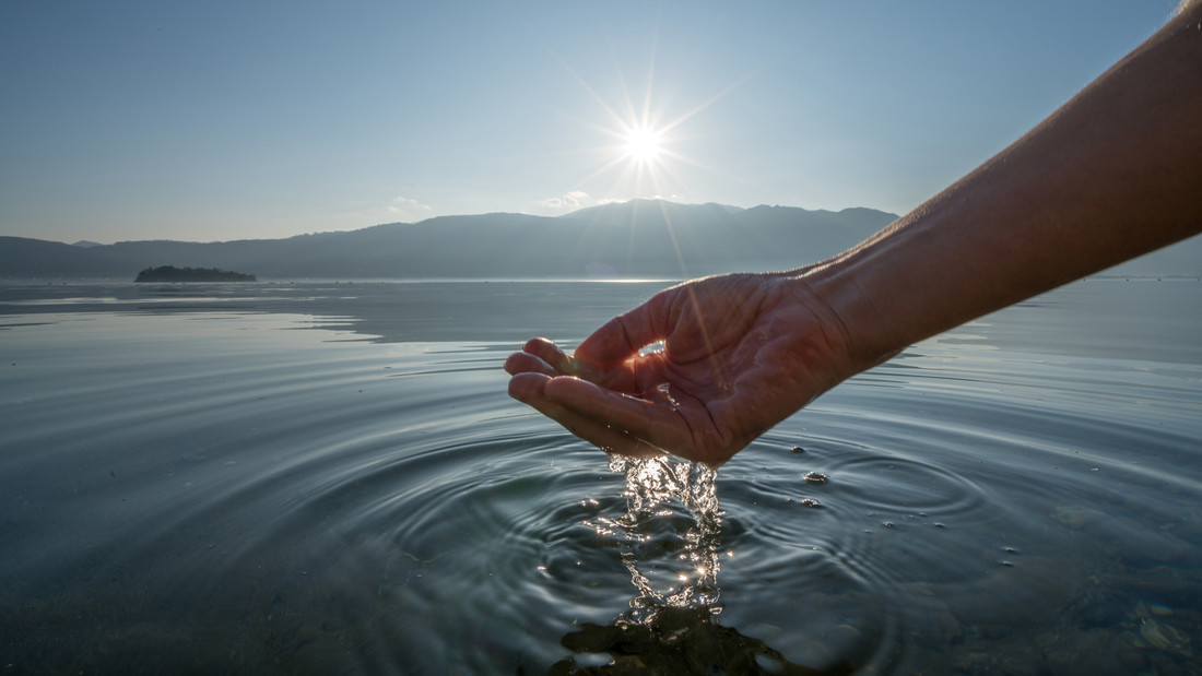Hand schöpft Wasser aus einem See