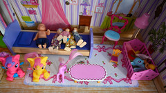 In einer Puppenstube ist ein kleine Bett mit Puppen drauf und andere kleine Spielzeuge zu sehen.