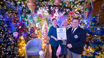 Susanne und Thomas Jeromin stehen mit Olaf Kuchenbecker (r) vom Rekord-Institut für Deutschland inmitten von Weihnachtsbäumen in ihrem Haus .