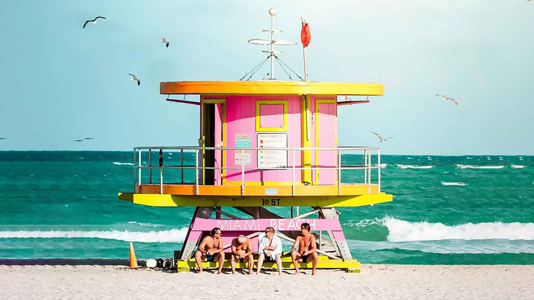 Personen sitzen vor einem Rettungsschwimmertur in Miami am Meer.