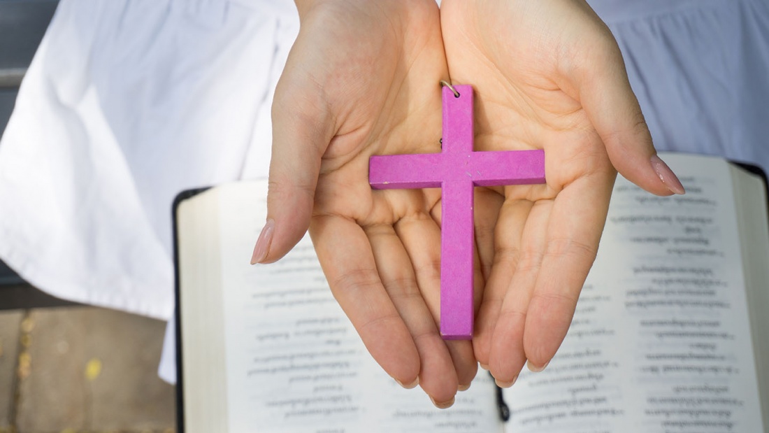 Frau hält rosa Kreuz über Bibel