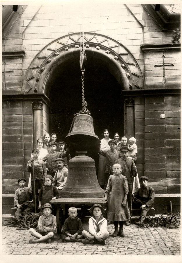 Eine Kinderschar steht und sitzt um zwei Glocken herum.