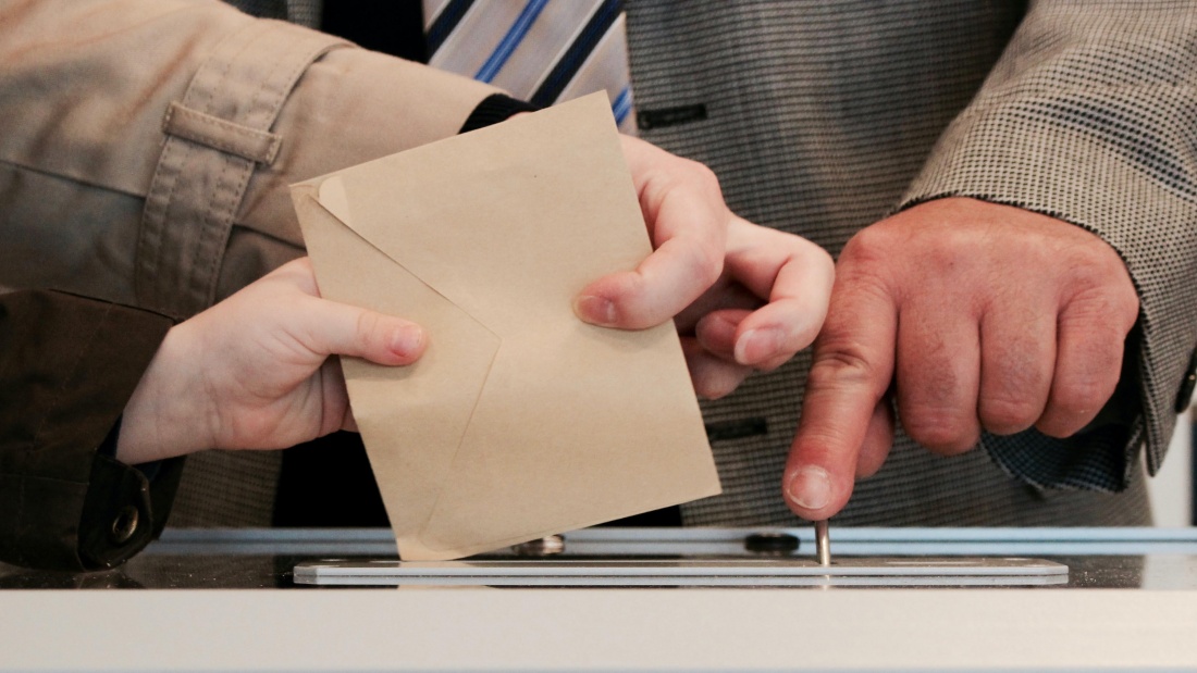 Hände verschiedener Generationen stecken einen Wahlbrief in die Urne