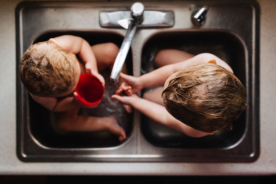 Zwei kleine Mädchen sitzen in einem Waschbecken und spielen miteinander.