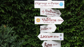 Ein Pilgerwegweiser mit vielen Schildern, die in verschiedene Richtungen zeigen, nach Rom oder Trondheim.