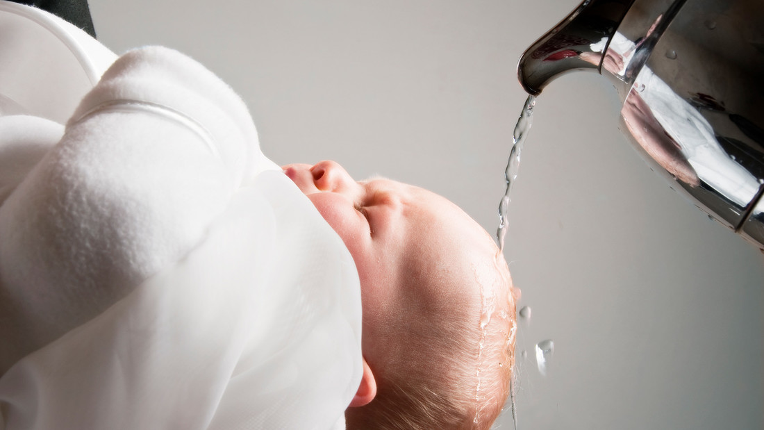 Ein Baby wird getauft und bekommt Wasser über die Stirn gegossen