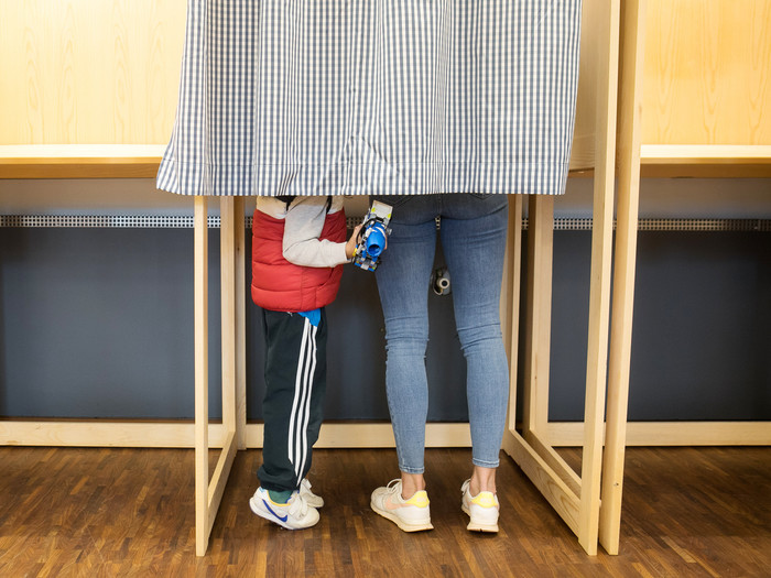Ob der Sohn ihr sagt, wen er wählen würde? Und warum? Mutter mit Kind in einer Wahlkabine in Miesbach 